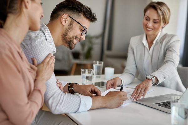 Young man signing a contract while being with his wife on a meet Happy man and his wife having a meeting with financial advisor and signing an agreement in the office.